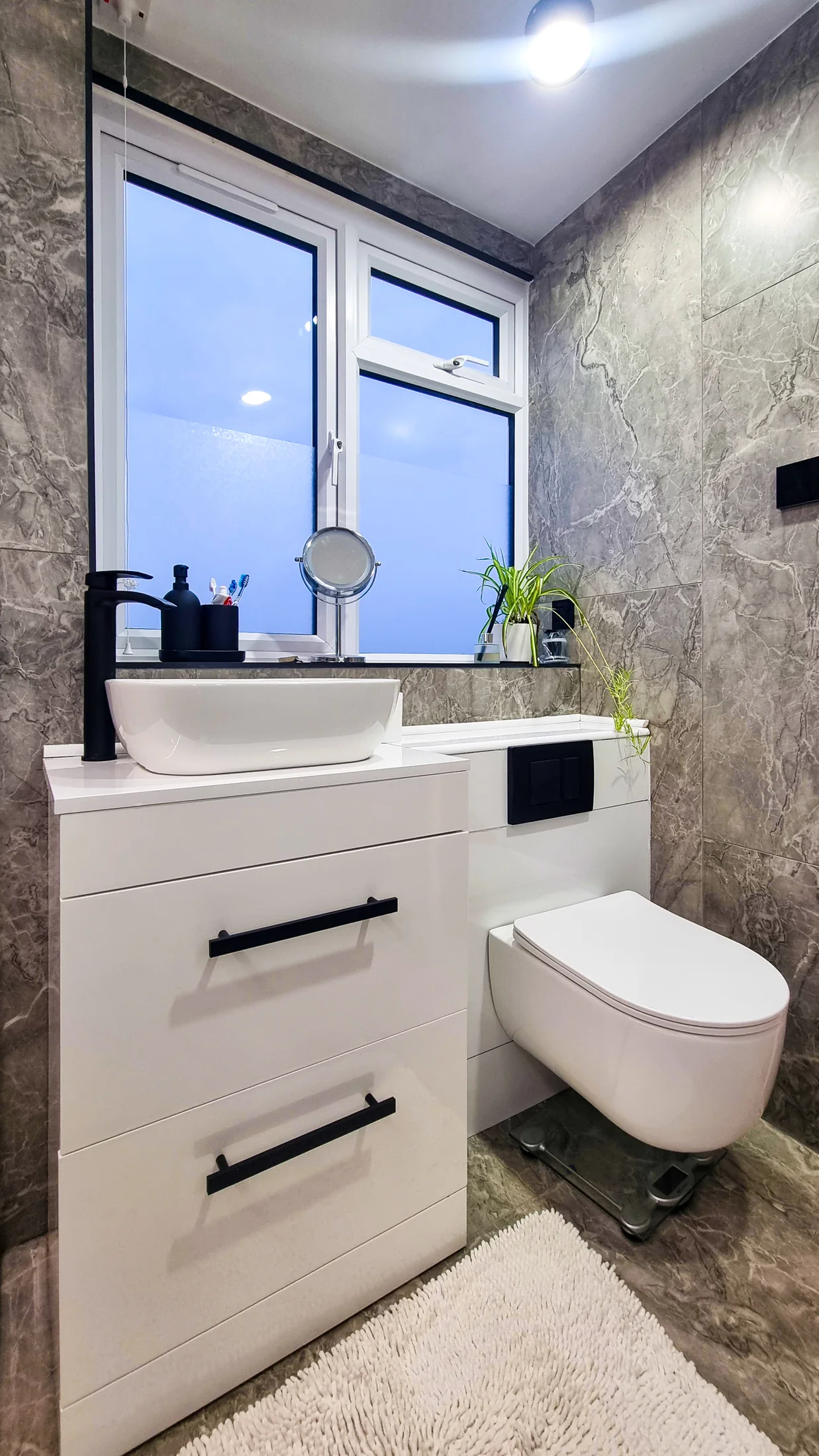 White vanity and wall-hung WC against marble-effect tiles