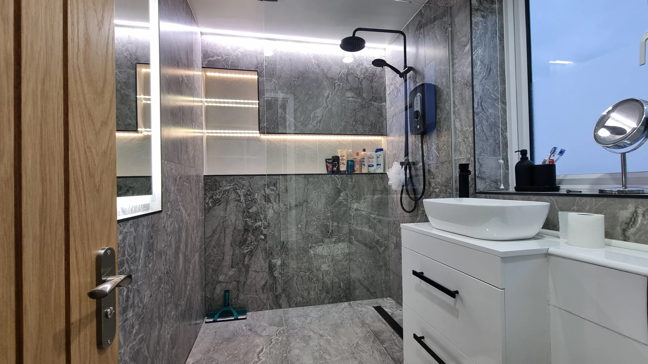 Completed dark marble-effect bathroom with illuminated recesses and white vanity